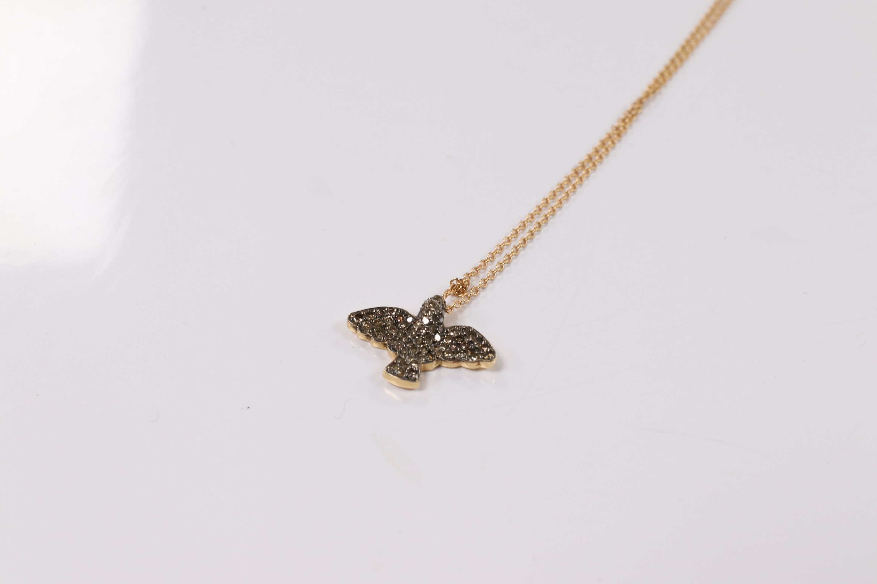 A modern 18k and pave set two colour diamond chip bird pendant, wing span 19mm, on an Italian 18k fine link chain, 36cm, gross weight 4.4 grams. Condition - fair to good